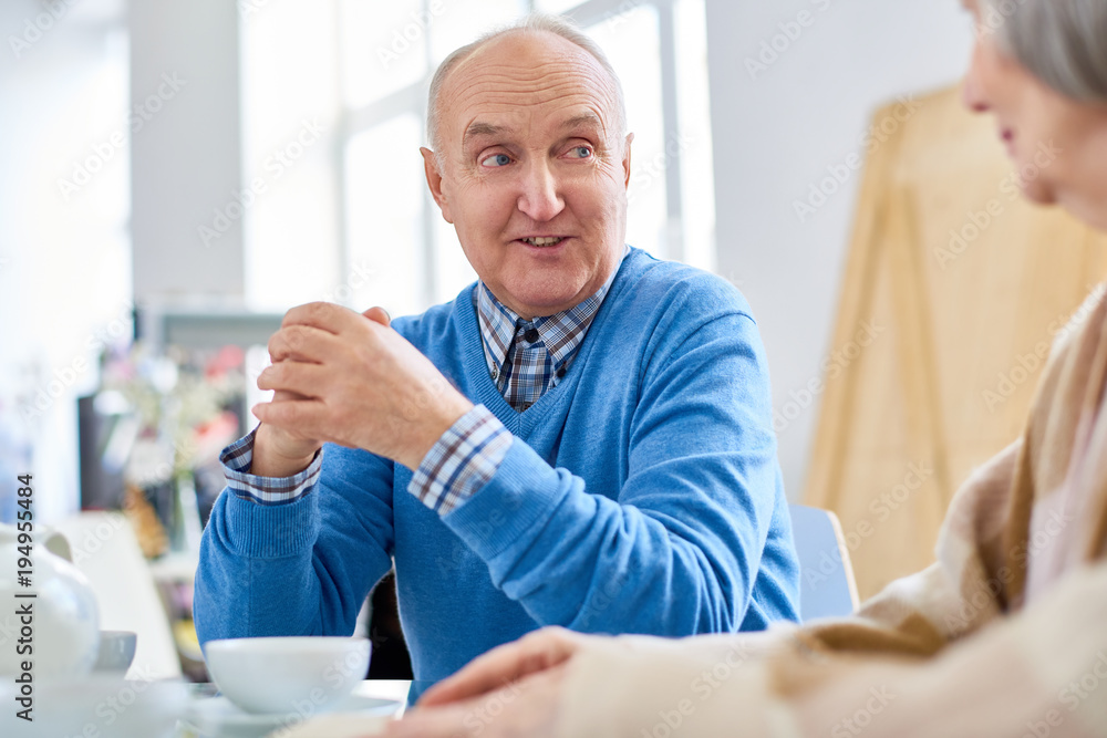 Portrait of nice senior couple enjoying conversation while drinking tea at home, focus on balding elderly man talking to wife, copy space Portrait of nice senior couple enjoying conversation while drinking tea at home, focus on balding elderly man talking to wife, copy space