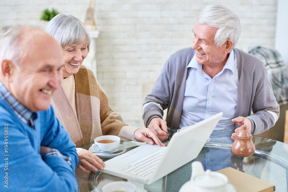 Portrait of three modern senior people using laptop in retirement home and smiling happily, copy space Portrait of three modern senior people using laptop in retirement home and smiling happily, copy space