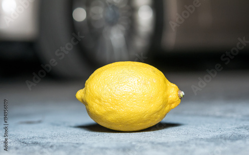 Lemon sitting on its side with the partial view of a car blurred in the background.