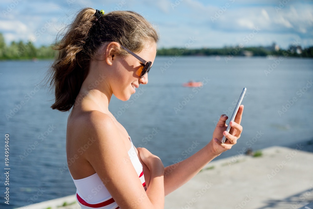 Young teenage girl shoots video on a smartphone for her channel. On a sunny summer day, in the city park