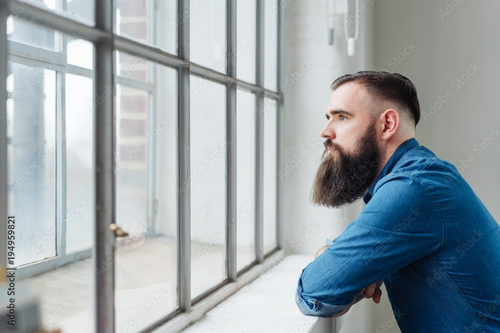 Thoughtful bearded man staring out of a window Thoughtful bearded man staring out of a window