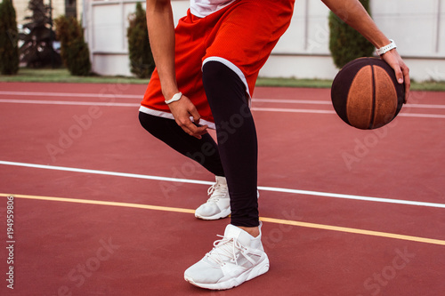 Team player. Close up part of young man in sportswear playing basketball on basketball court outdoors
