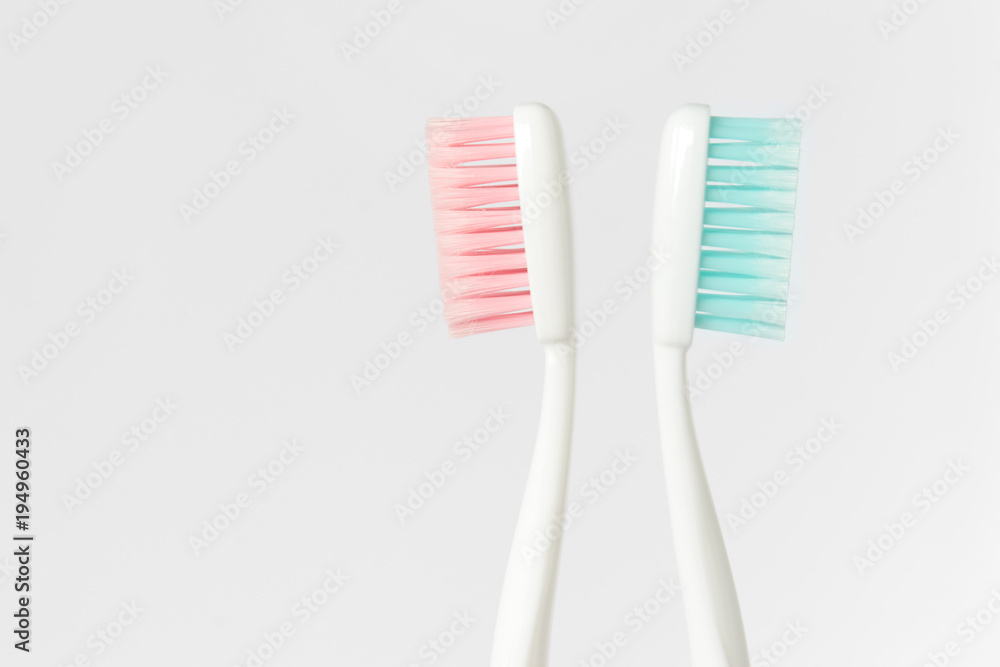 Close up of two plastic white toothbrushes with pink and blue bristle on white background. Free copy space. Close up of two plastic white toothbrushes with pink and blue bristle on white background. Free copy space.