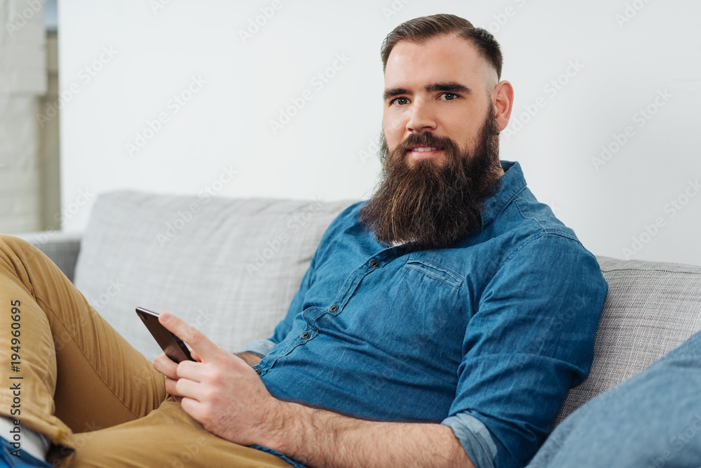 Smiling bearded man with mobile phone on sofa