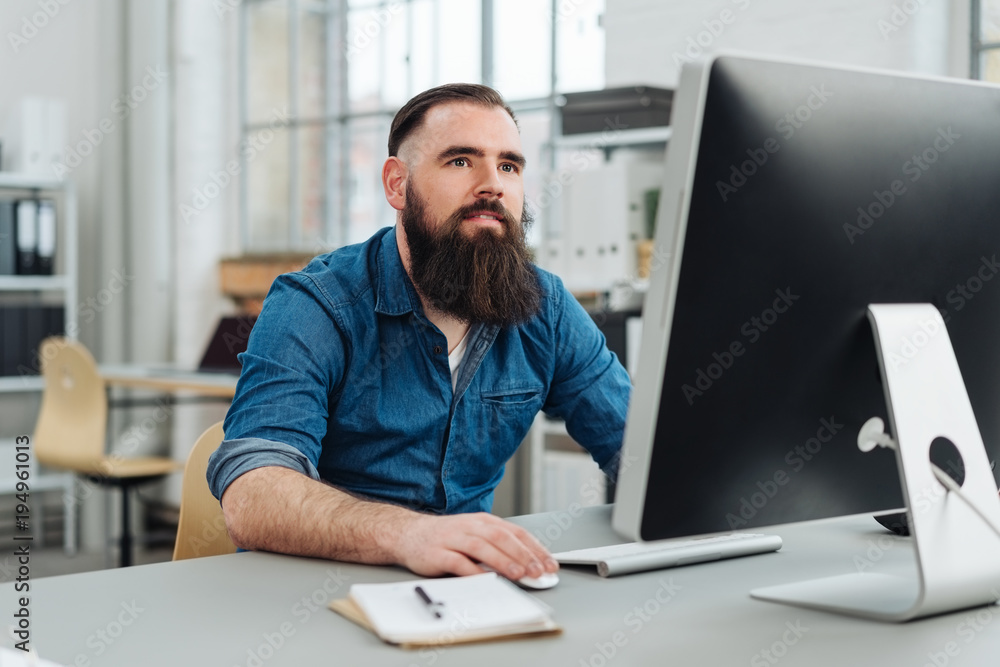 Bearded man sitting in front of monitor at office