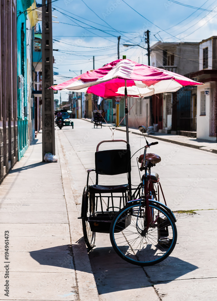 Obraz premium Bicycle taxi, pedicab bike parked on the side of a street. Colorful umbrella attached to the cart to provide shade for riders.