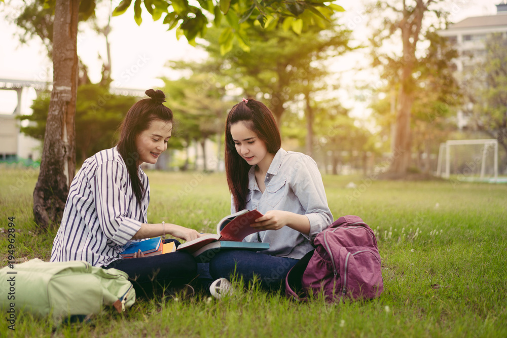 Young women together study reading book in university and knowledge at outside or park campus relaxing smile in summer season Young women together study reading book in university and knowledge at outside or park campus relaxing smile in summer season