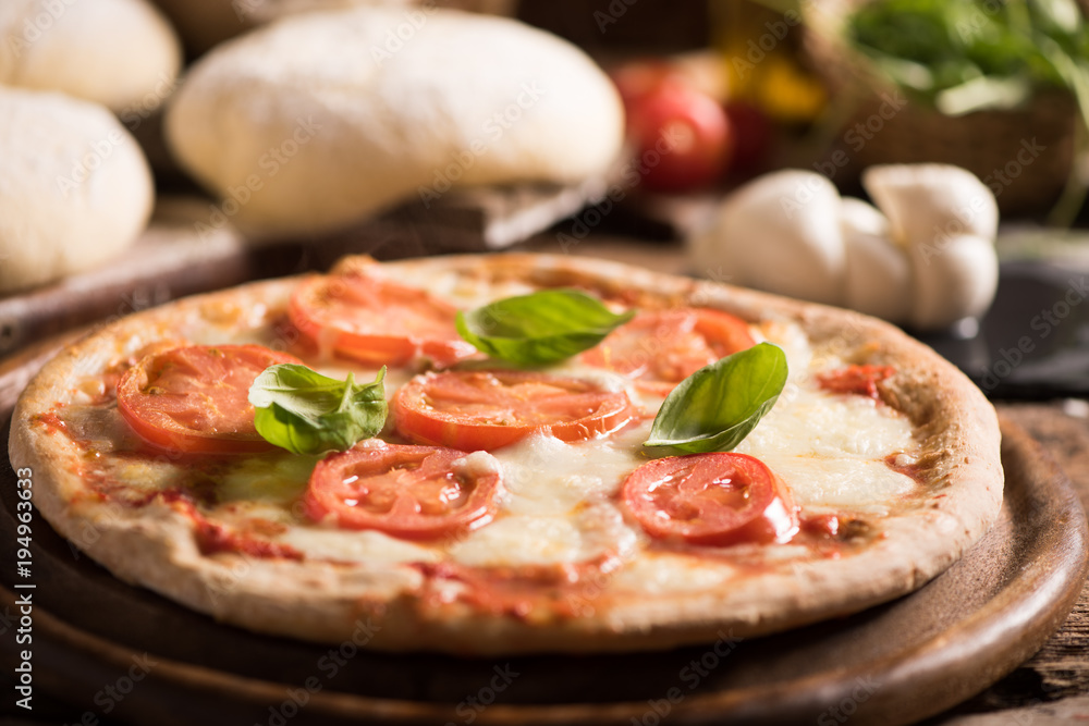 Italian pizza with tomato topped with melted golden cheese, herbs and basil served on a round wooden board on an old wood table