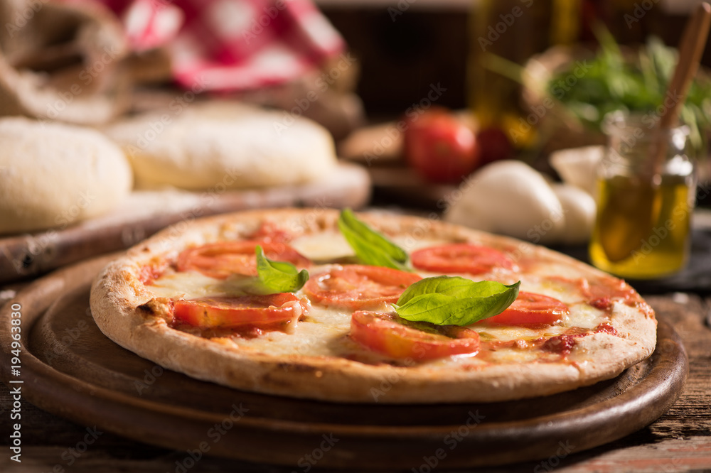 Italian pizza with tomato topped with melted golden cheese, herbs and basil served on a round wooden board on an old wood table