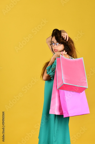 Girl stands on yellow background, holds pink shopping bags