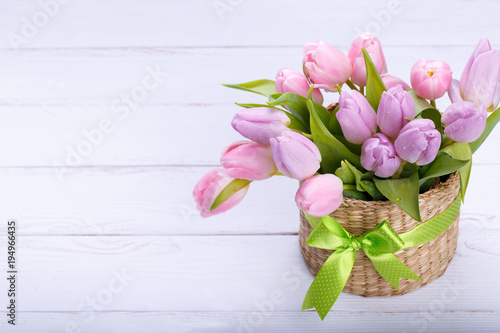 Fototapeta Naklejka Na Ścianę i Meble -  Bouquet of pink tulips in a wicker basket on light gray background