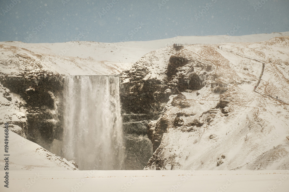Fototapeta premium Skogafoss, the great and beautiful waterfall in Iceland during winter. Snow blizzard in Iceland near famous Skogafoss waterfall.