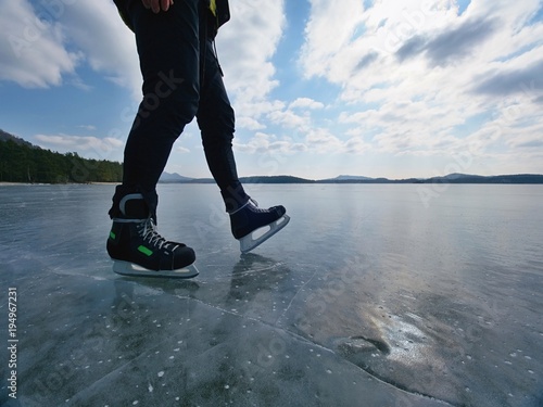 Man ice skating on frozen lake. Thin ice with deeep cracks below man photo