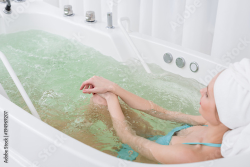 Tableau sur toile side view of woman in swimming suit with towel on head relaxing in bath in spa s