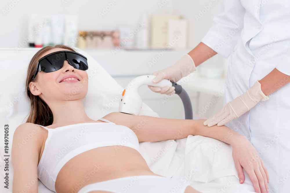 cropped shot of woman getting laser hair removal procedure on arm in salon cropped shot of woman getting laser hair removal procedure on arm in salon