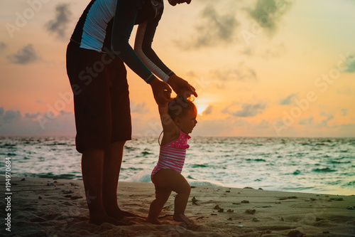 father and little daughter walking on sunset beach