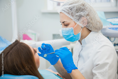 Female stomatologist in blue protective mask examining patient s teeth. Dentist caries treatment at dental clinic office. People  medicine  stomatology and health care concept
