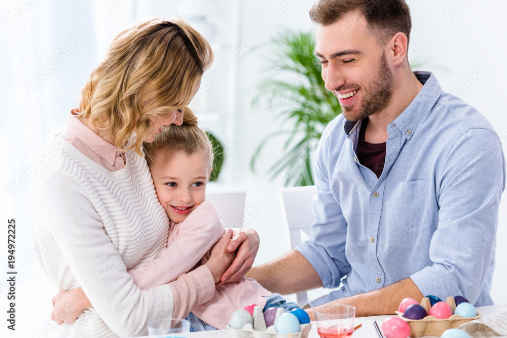 Fototapeta premium Cheerful family embracing by painted eggs for Easter