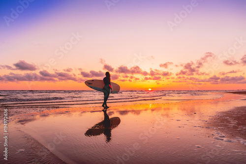 Silhouette and reflection of surfer girl with surfboard on a beach at sunset. Surfer and ocean photo