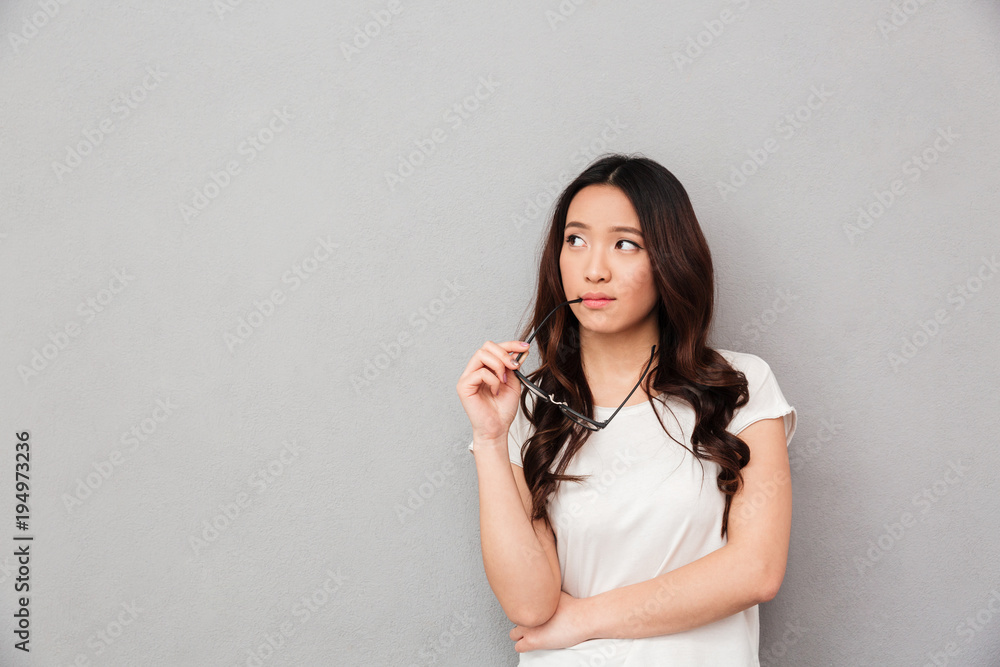 Pensive asian woman in t-shirt holding eyeglasses and looking away Pensive asian woman in t-shirt holding eyeglasses and looking away