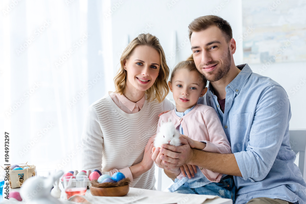 Happy family holding Easter rabbit with painted eggs on table Happy family holding Easter rabbit with painted eggs on table