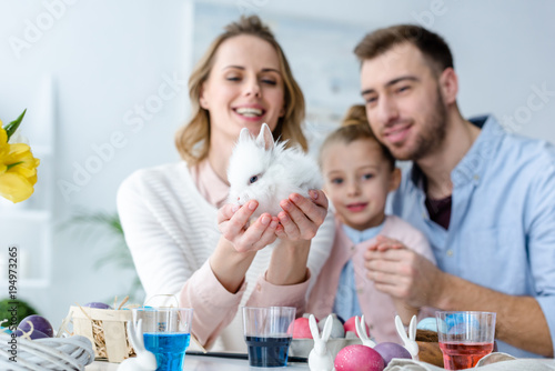 Mother with family holding cute bunny by table with Easter eggs