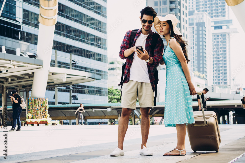 Fototapeta premium Couple Asian travelers are walking on city street and looking at interesting places to travel from smart phone. Vacation and technology Concept