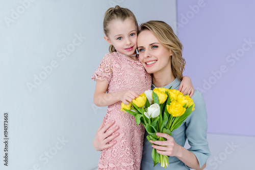 Woman holding bouquet and embracing cute daughter on women's day