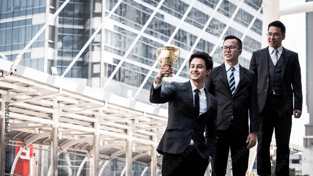 Happy Asian business people with golden trophy cup for their winner in business project. Teamwork and success concept Happy Asian business people with golden trophy cup for their winner in business project. Teamwork and success concept