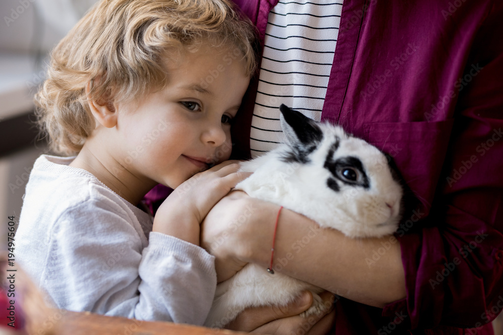 Close up portrait of cute blond toddler hugging pet bunny and clinging to mom Close up portrait of cute blond toddler hugging pet bunny and clinging to mom