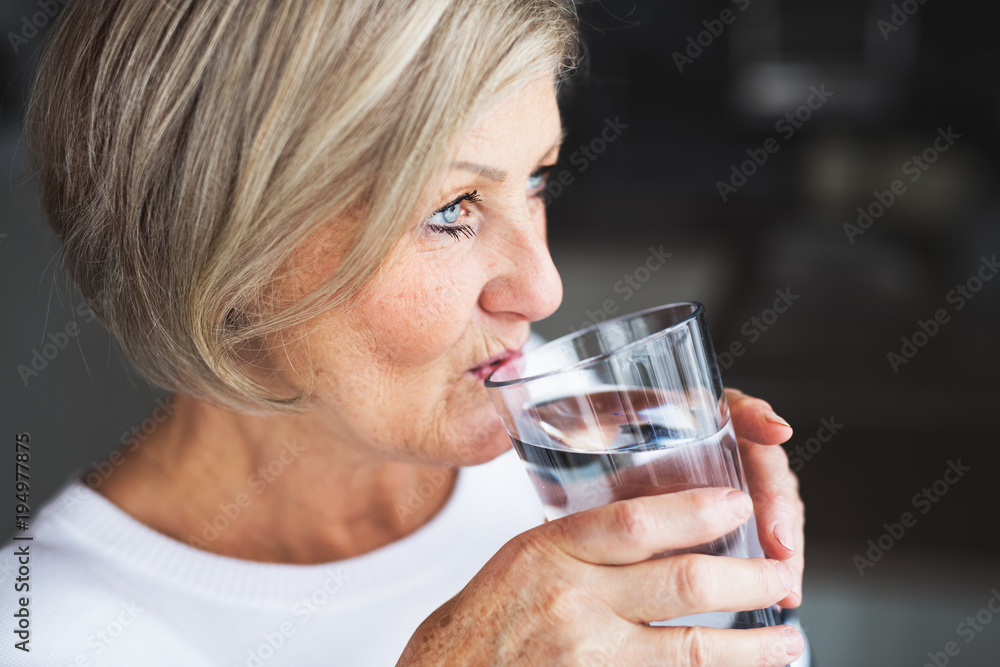 Senior woman drinking water in the kitchen. Senior woman drinking water in the kitchen.