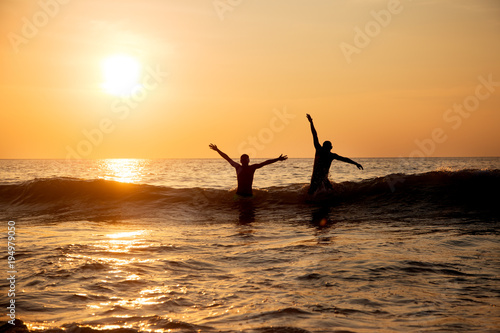 two men are floating on waves in the sea at sunset 