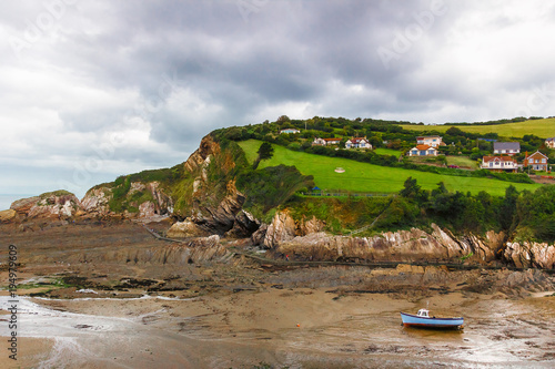 Felsenküste an der englischen Meerseite von Devon. Es ist Ebbe. Boote liegen auf Sand.