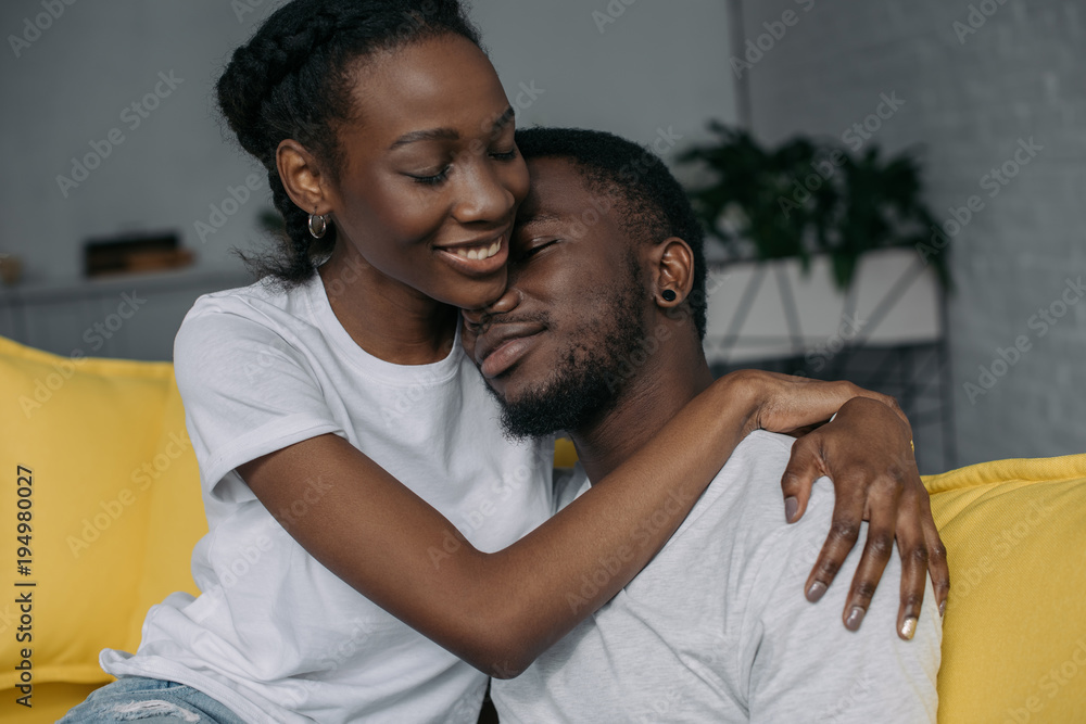 Obraz premium beautiful happy young african american couple in white t-shirts hugging at home