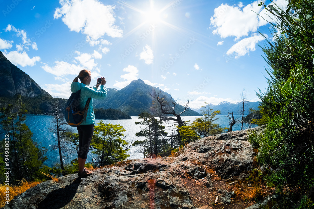 Woman hiker takes a pictures of a valley with lake and mountains. Patagonia, Argentina