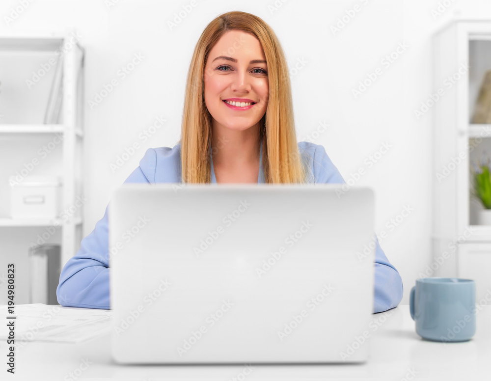 Attractive blonde in a blue business suit in a bright office working on a laptop. Attractive blonde in a blue business suit in a bright office working on a laptop.