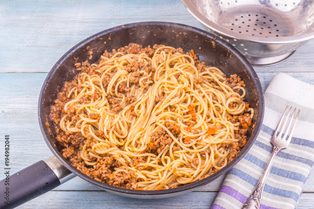 Spaghetti bolognese in a frying pan on a rustic background and colander Spaghetti bolognese in a frying pan on a rustic background and colander