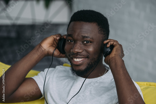 handsome african american man listening music in headphones and smiling at camera