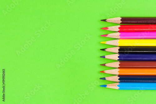 Row of colorful wooden pencils on background of green paper. Top view