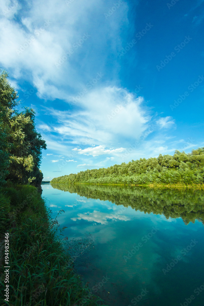 Riverbank of calm Danube river with green trees in spring or summer and deep blue sky with clouds at the setting sun. Ukraine