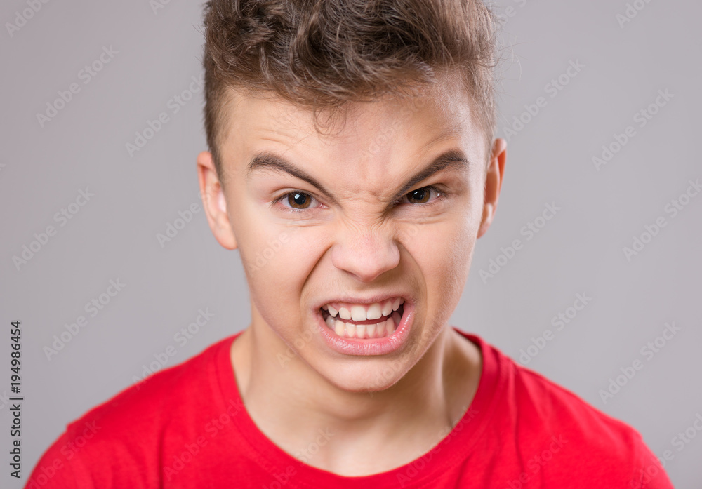 Emotional portrait of irritated shouting teen boy. Furious teenager screaming and looking with anger at camera. Handsome outraged child shouting out loud on gray background. Emotional portrait of irritated shouting teen boy. Furious teenager screaming and looking with anger at camera. Handsome outraged child shouting out loud on gray background.