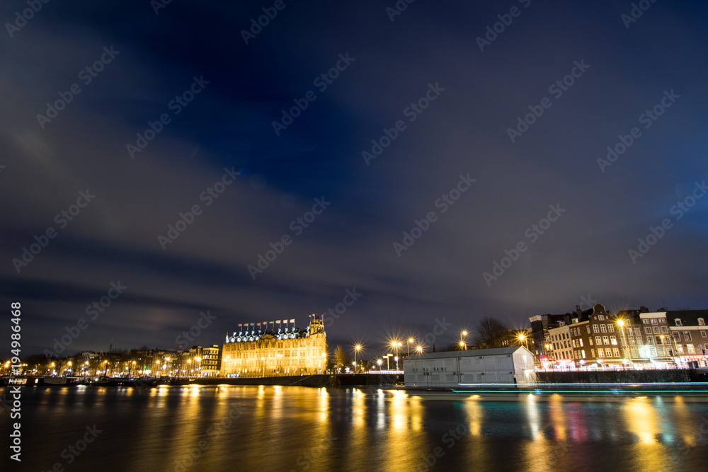 Night view of an Amsterdam canal from the central station with a boat leaving its luminous wake