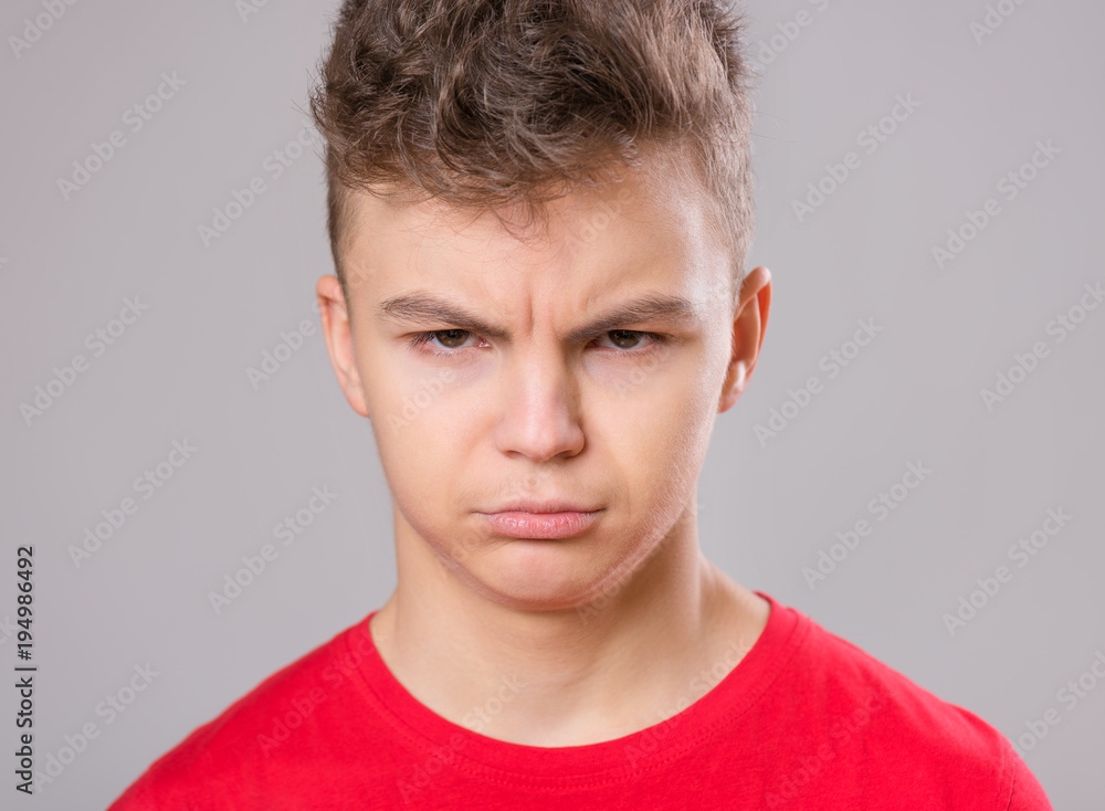 Close up emotional portrait of caucasian upset problem teen boy. Sad boy looking at camera. Worried child wearing red t-shirt, on gray background. Close up emotional portrait of caucasian upset problem teen boy. Sad boy looking at camera. Worried child wearing red t-shirt, on gray background.