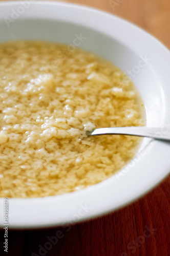 Typical German homemade chicken broth with tiny, Italian star-shaped noodles, called Stelline, in white soup plate with spoon as prevention or remedy when having a cold