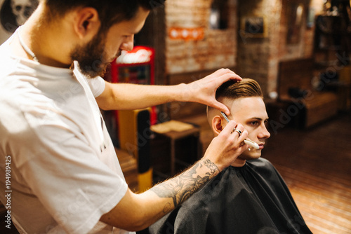 Making hair look magical. Young bearded man hairdresser at barbershop. Soft focus, noise