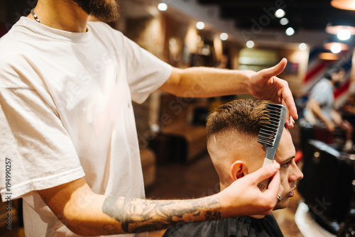 Creating new hair look. Making haircut look perfect. Young bearded man getting haircut by hairdresser while sitting in chair at barbershop