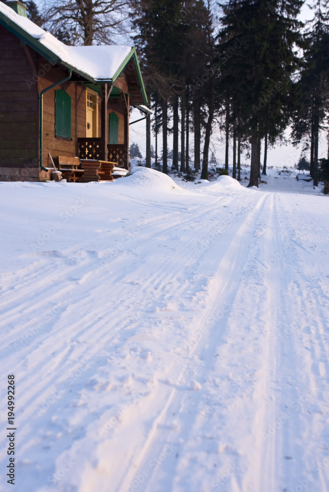 Skispur Langlauf Loipe mit Berghütte am Abend im Wald Skispur Langlauf Loipe mit Berghütte am Abend im Wald