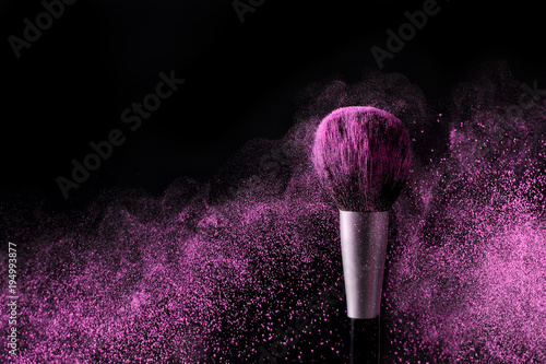 Brush for makeup with purple make-up shadows in motion on a black background.
