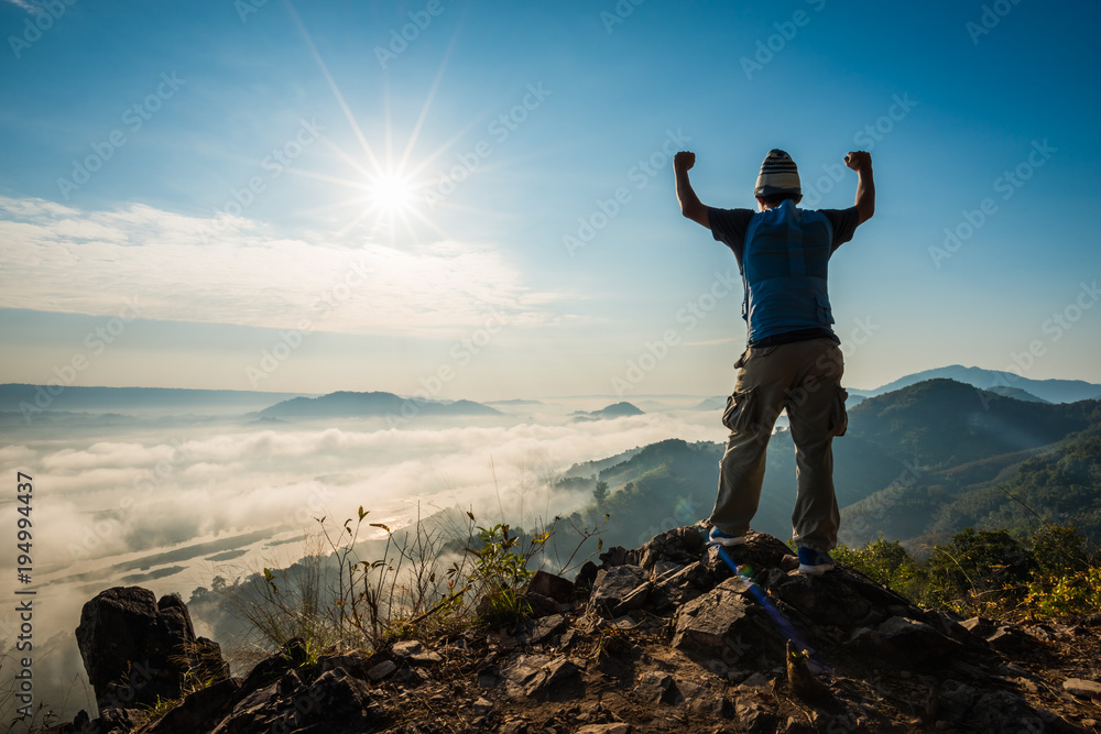 Silhouette man standing on top of the mountain watching the sun rise with fog Silhouette man standing on top of the mountain watching the sun rise with fog