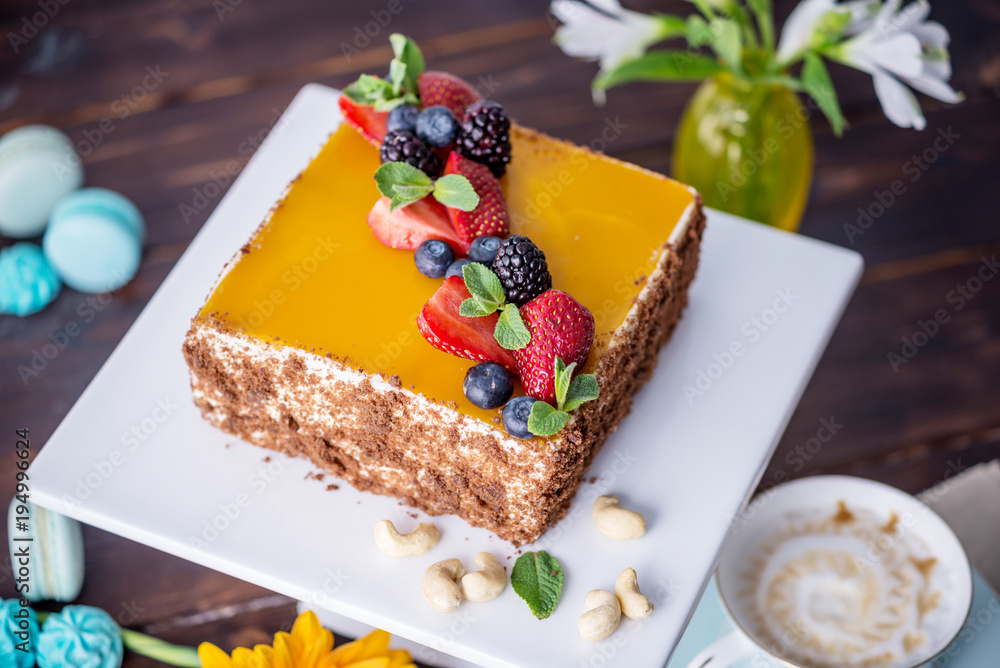 Homemade square cake decorated with yellow jelly on top and berries with mint on dark background Homemade square cake decorated with yellow jelly on top and berries with mint on dark background
